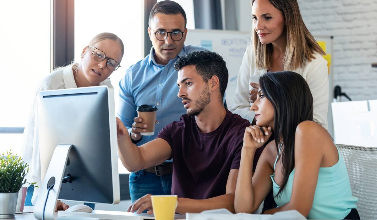 successful-business-team-standing-around-computer-Z47XJL5.jpg